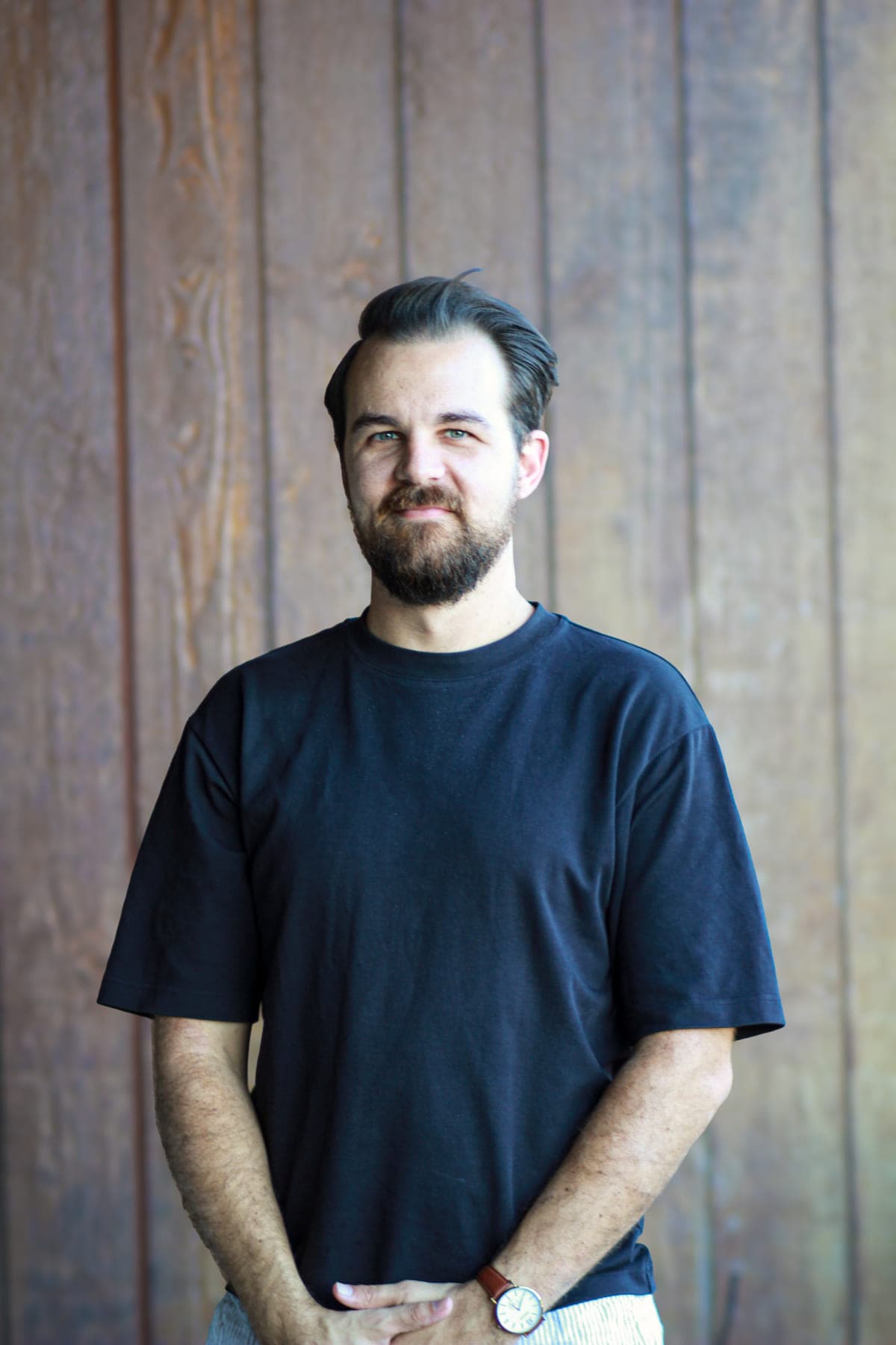 Cameron Radburn standing in front of a timber wall, hands in his pockets, relaxed and smiling.