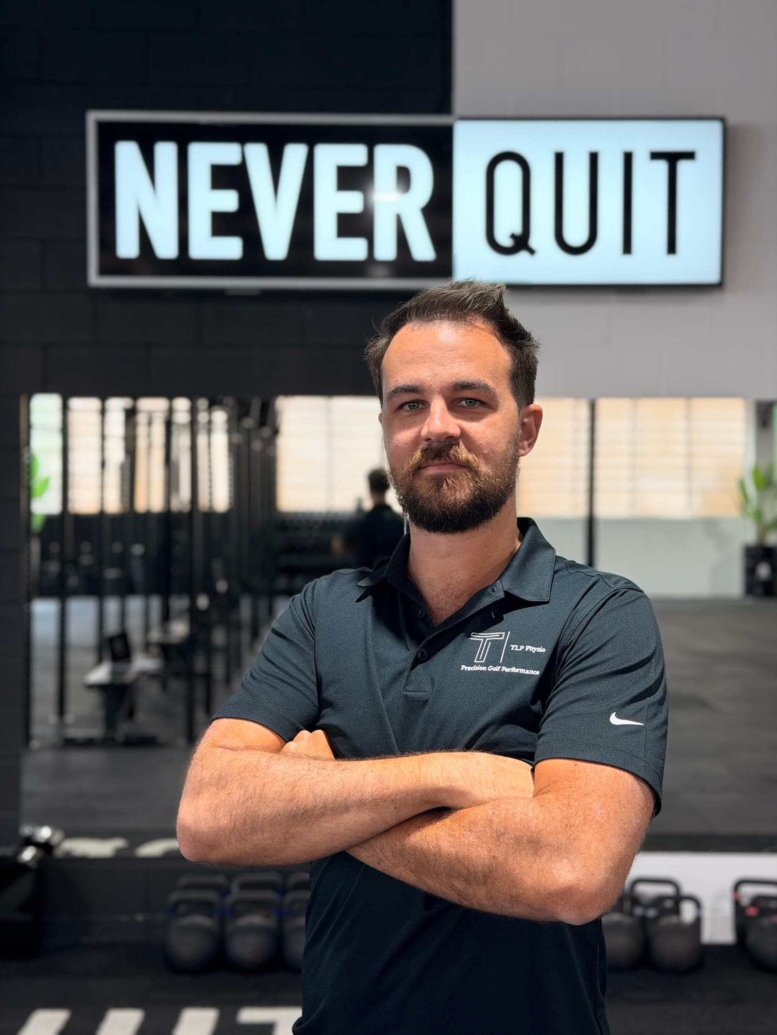 Cameron Radburn, Physiotherapist, standing in the gym floor at Never Quit South Brisbane beneath the Never Quit sign.