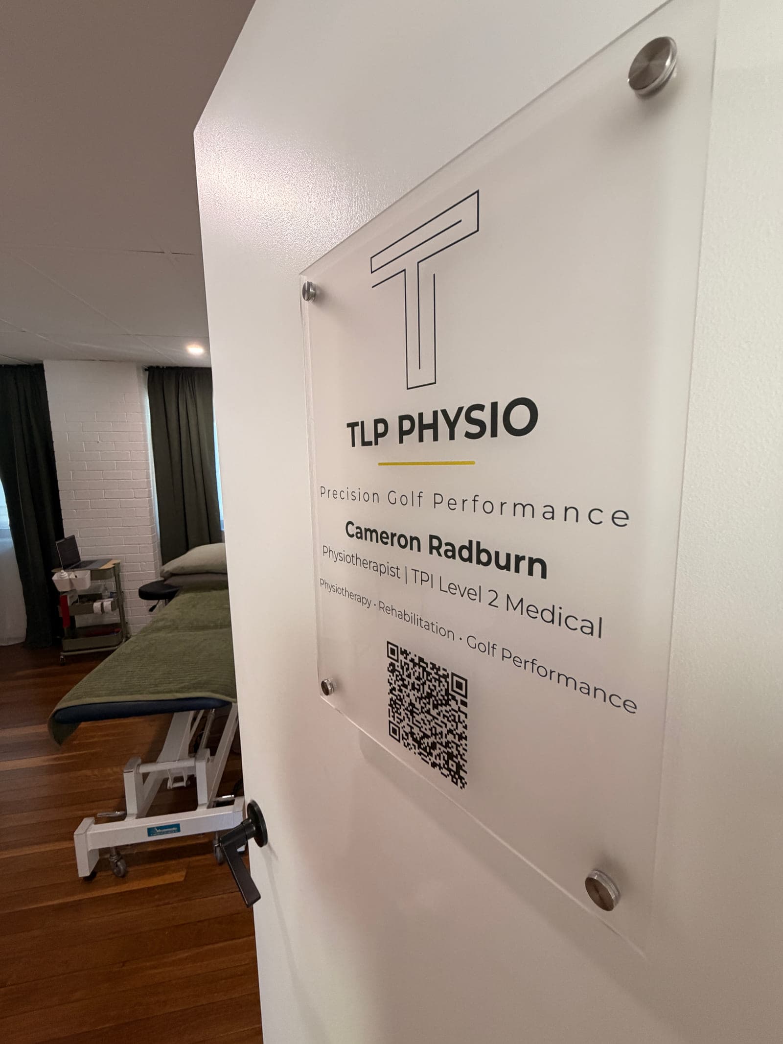 The open TLP Physio treatment-room door inside Never Quit South Brisbane, with the TLP Physio sign on the door and the treatment room visible through the doorway.