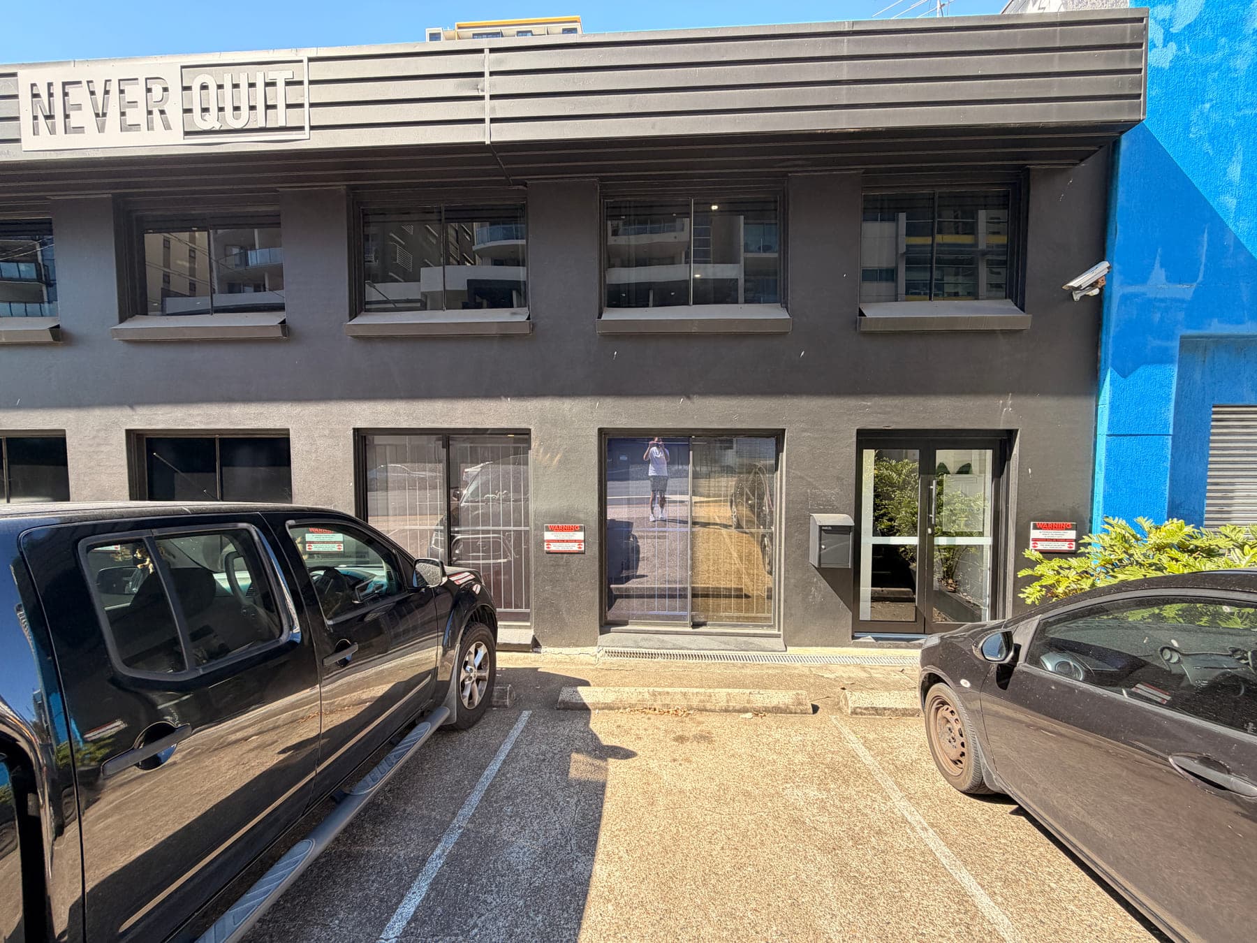 The Never Quit South Brisbane building on Merivale Street, with the Never Quit sign above the entrance and parking directly in front.