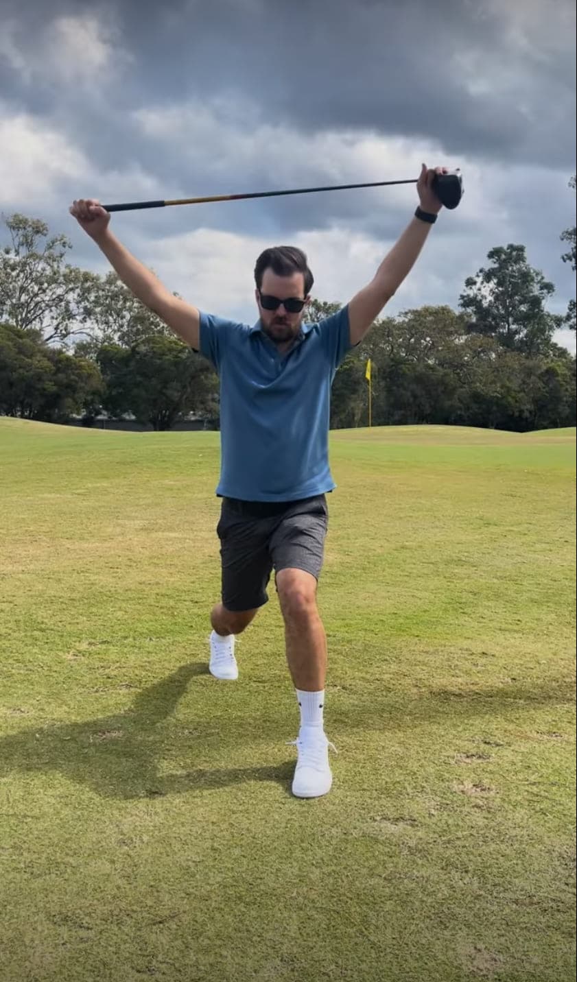 Cameron Radburn on a golf course in a reverse lunge, holding a driver overhead with both arms extended.