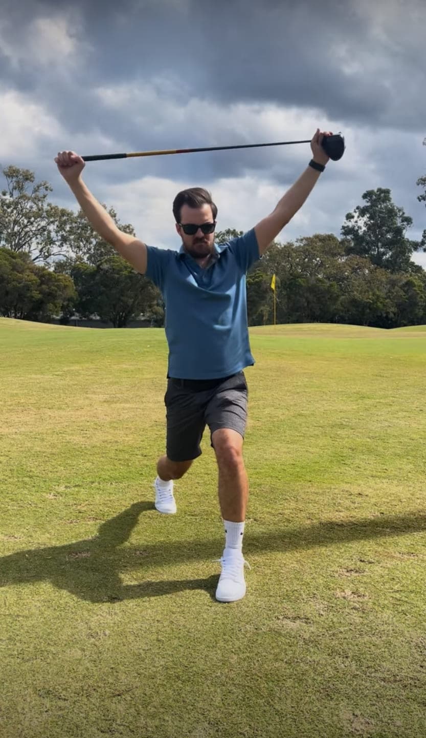 Cameron Radburn on a golf course in a reverse lunge, holding a driver overhead and looking toward the camera.